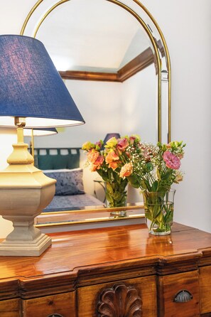 Une commode en bois, sur laquelle sont posés une lampe et deux vases en verre remplis de fleurs.