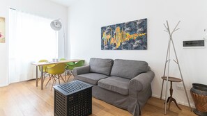 Un salon avec un canapé gris, une table à manger avec des chaises, un lampadaire et un tableau accroché au mur.