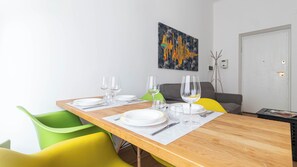 Un coin repas avec une table en bois, des chaises vertes et jaunes, et un tableau accroché au mur.