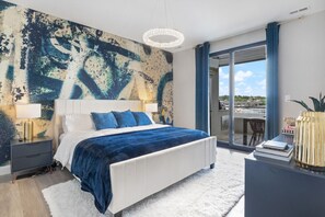 Relax in this serene bedroom with a large bed, nightstand, and dresser, surrounded by a beautiful abstract painting and a potted plant.