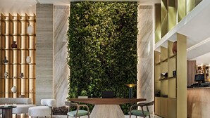 Een modern interieur met een hoge plafond, een groene wand met planten, een receptiebalie en een zithoek met stoelen en een tafel.