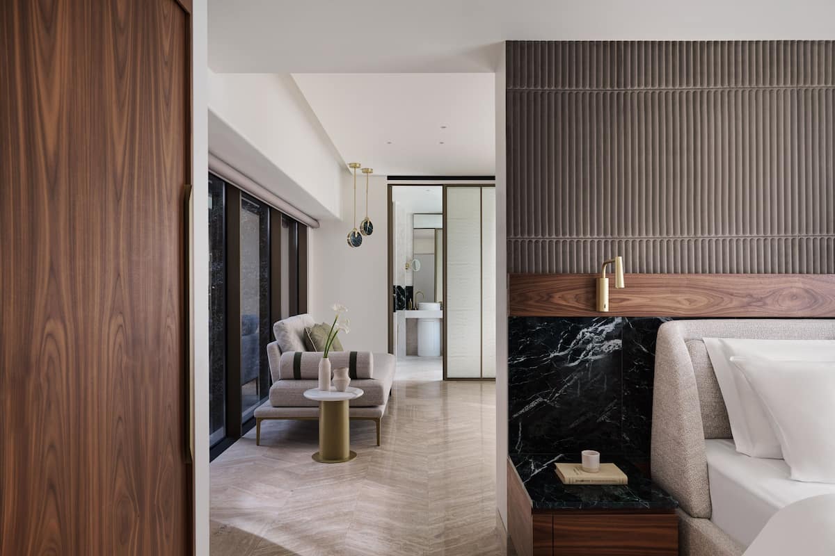 A modern hotel room with a large bed, a small side table, a sofa, and a view of the city.