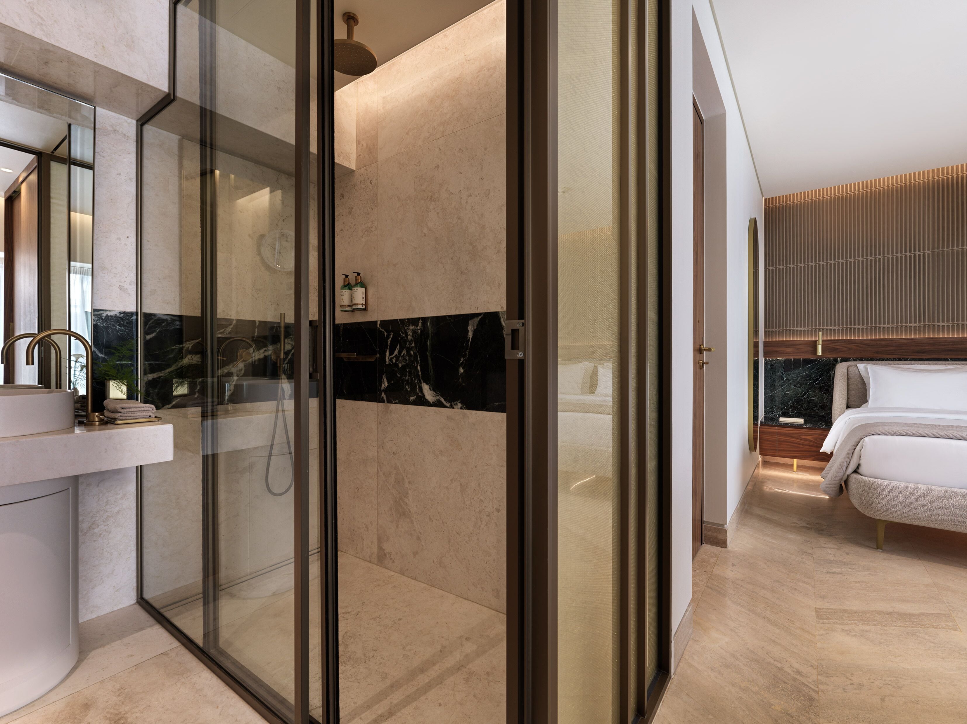 A modern bathroom with a glass-enclosed shower, a marble-tiled wall, and a large mirror.