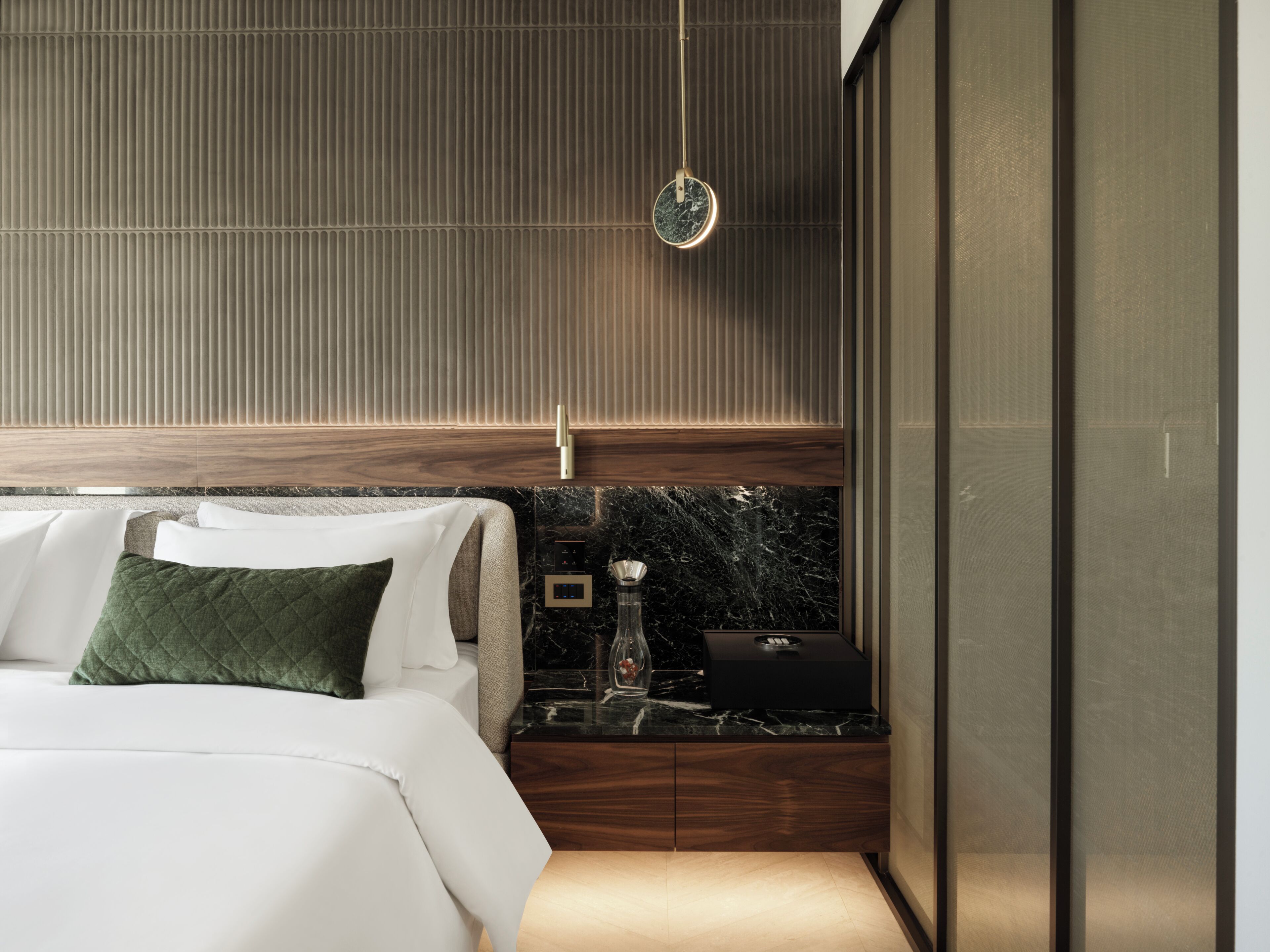 Une chambre à coucher moderne avec un lit, une table de chevet, une tête de lit en marbre et un luminaire fixé au mur.