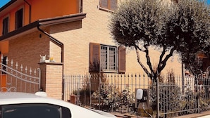 A white car parked in front of a building with a brick facade, a metal fence, and a tree. - Villa Patty Assisi with SPA Billiards, Table Football. 2-12 People, Pet Friendly (Castelnuovo)