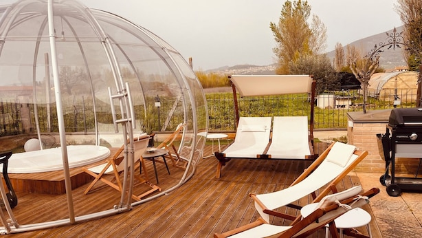 A covered outdoor seating area with wooden flooring, lounge chairs, and a transparent dome structure. - Villa Patty Assisi with SPA Billiards, Table Football. 2-12 People, Pet Friendly (Castelnuovo)