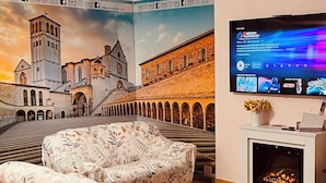A living room with a large mural of a historic building, a flat-screen TV, and a fireplace. - Villa Patty Assisi with SPA Billiards, Table Football. 2-12 People, Pet Friendly (Castelnuovo)