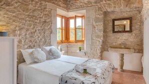 A bedroom with a stone wall, a wooden bed, a window with wooden shutters, a stone sink, and a mirror. - Flateli El Racó de Diana (Sant Jordi Desvalls)