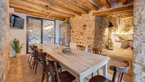 A rustic dining area with a wooden table and chairs, stone walls, and a stone fireplace. - Flateli El Racó de Diana (Sant Jordi Desvalls)