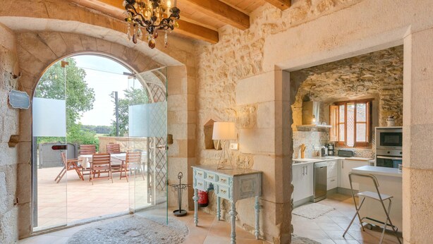 A rustic stone interior with a kitchen, dining area, and a view through an archway. - Flateli El Racó de Diana (Sant Jordi Desvalls)