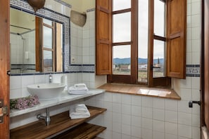 A bathroom with a white sink, wooden shelves, a mirror, and a window with wooden shutters.