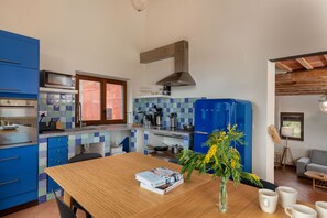 A kitchen with blue cabinets, a wooden table, and a vase with flowers. - Flateli. Casa Indiana (Bordils)