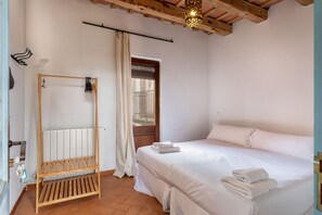 A bedroom with a wooden bed frame, white bedding, a radiator, and a hanging light fixture.