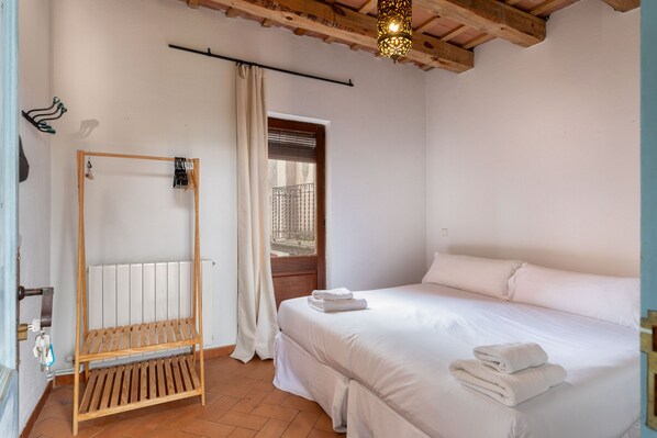 A bedroom with a wooden bed frame, white bedding, a radiator, and a hanging light fixture.