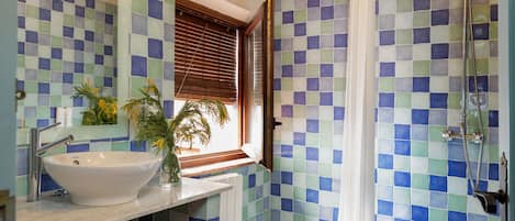 A bathroom with a large sink, a window with blinds, and a shower area.
