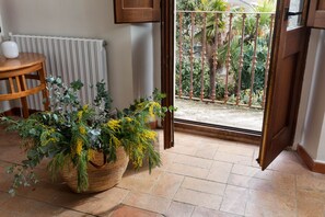 A room with a potted plant, a wooden table, and a view of a garden through an open door.