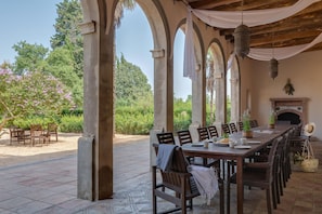An outdoor dining area with a long wooden table, multiple chairs, and a fireplace.