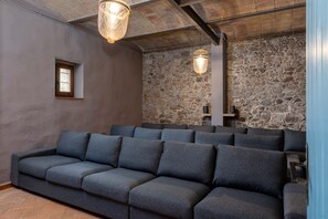 A modern cinema room with a stone wall backdrop, a dark grey sofa, and hanging lights.
