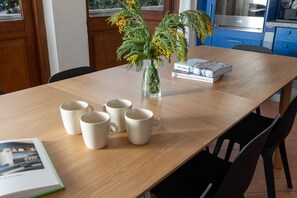 Une table à manger ornée d’un vase de fleurs jaunes, de plusieurs tasses blanches et d’un livre intitulé « L’amour et la nourriture ».