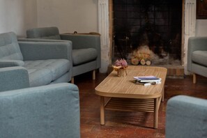 A living room with a fireplace, grey sofas, a wooden coffee table with books, and a vase with flowers.