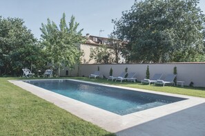 Une piscine rectangulaire dont le bord est recouvert de carreaux, entourée d’une pelouse verdoyante et de plusieurs chaises longues.