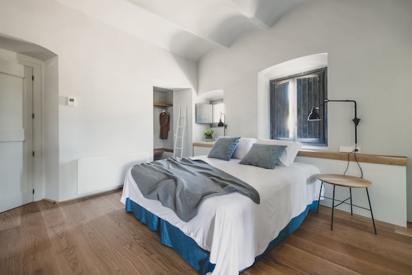 Une chambre avec un grand lit, un plancher en bois, une fenêtre donnant sur un beau paysage, une table de chevet et une armoire.