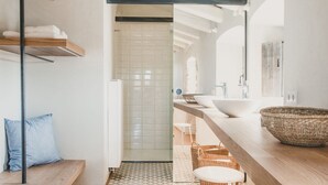 A modern bathroom with a geometric patterned floor, a wooden bench, a towel rack, and a large woven basket.
