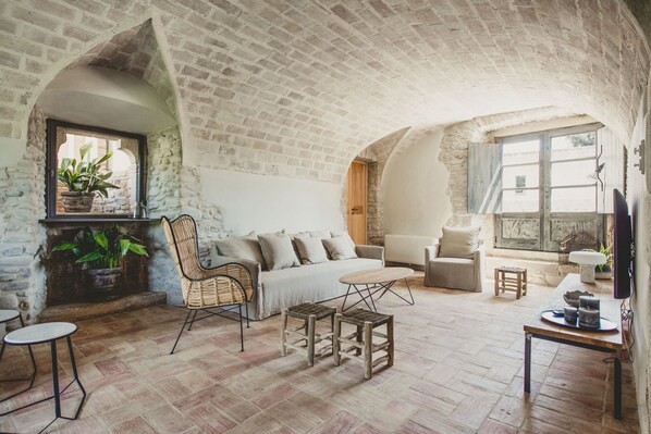 A rustic room with exposed brick walls, a stone fireplace, a sofa, a chair, and a small table.
