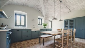 A kitchen with a large island, blue cabinets, and a rustic brick floor.
