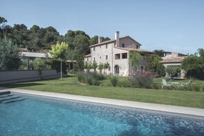 Una amplia casa con piscina, rodeada de un césped cuidado y diversas plantas.