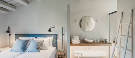 Un dormitorio con cama, mesita de noche, lámpara y un baño con lavamanos, espejo y toallero.
