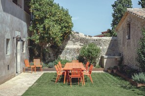 Un patio con mesa y sillas, un muro de piedra y un árbol con frutos.