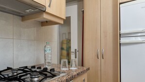 Een keuken met een gasfornuis, een granieten aanrechtblad, houten keukenkastjes en een witte koelkast.