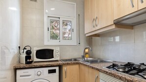 Een praktische keuken met een wasmachine, magnetron, fornuis en een raam met uitzicht op bomen.
