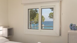 Een slaapkamer met een groot raam dat uitzicht biedt op zee en bomen.