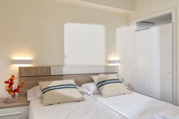A hotel room with a bed, bedside lamps, a nightstand, a vase with flowers, and a wardrobe.