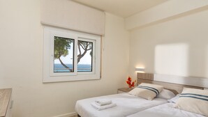 A bedroom with two beds, a window with a view of the sea, and a nightstand with a vase of flowers. - Flateli. PDA Vista Mar 2 (Platja d´Aro)
