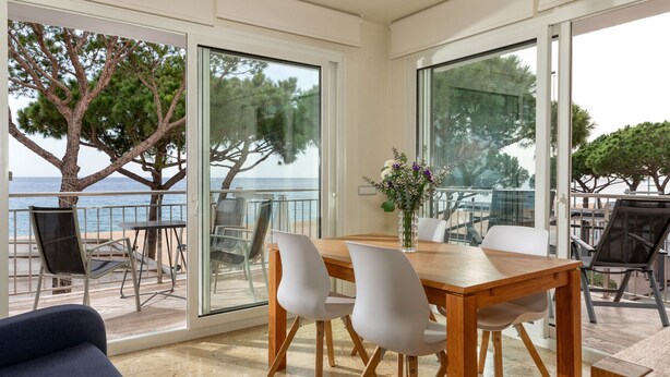 A dining area with a wooden table and white chairs, large glass doors leading to a balcony with a view of the sea and trees. - Flateli. PDA Vista Mar 3 (Platja d´Aro)