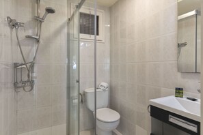 Un baño moderno con ducha de vidrio, inodoro blanco y lavamanos con espejo.
