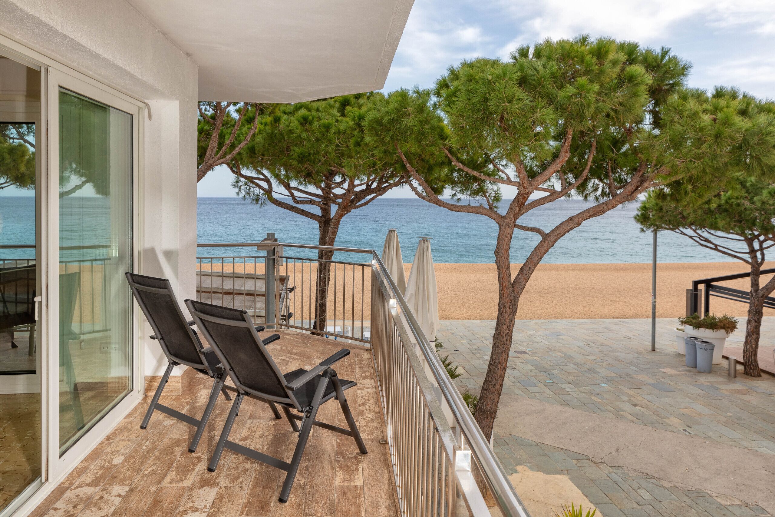 A balcony with two chairs, a railing, and a view of the beach and sea.