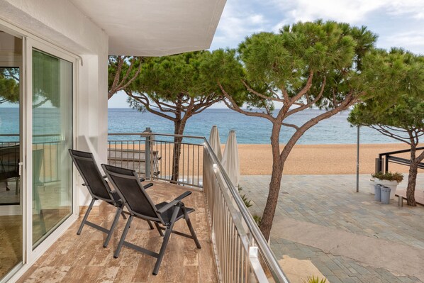 A balcony with two chairs, a railing, and a view of the beach and sea.