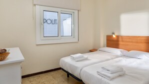 A hotel room with two beds, a window with a view, a bedside table, and a basket on the desk. - Flateli. PDA Vista Mar 3 (Platja d´Aro)