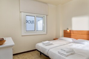 A hotel room with two beds, a window with a view, a bedside table, and a basket on the desk.