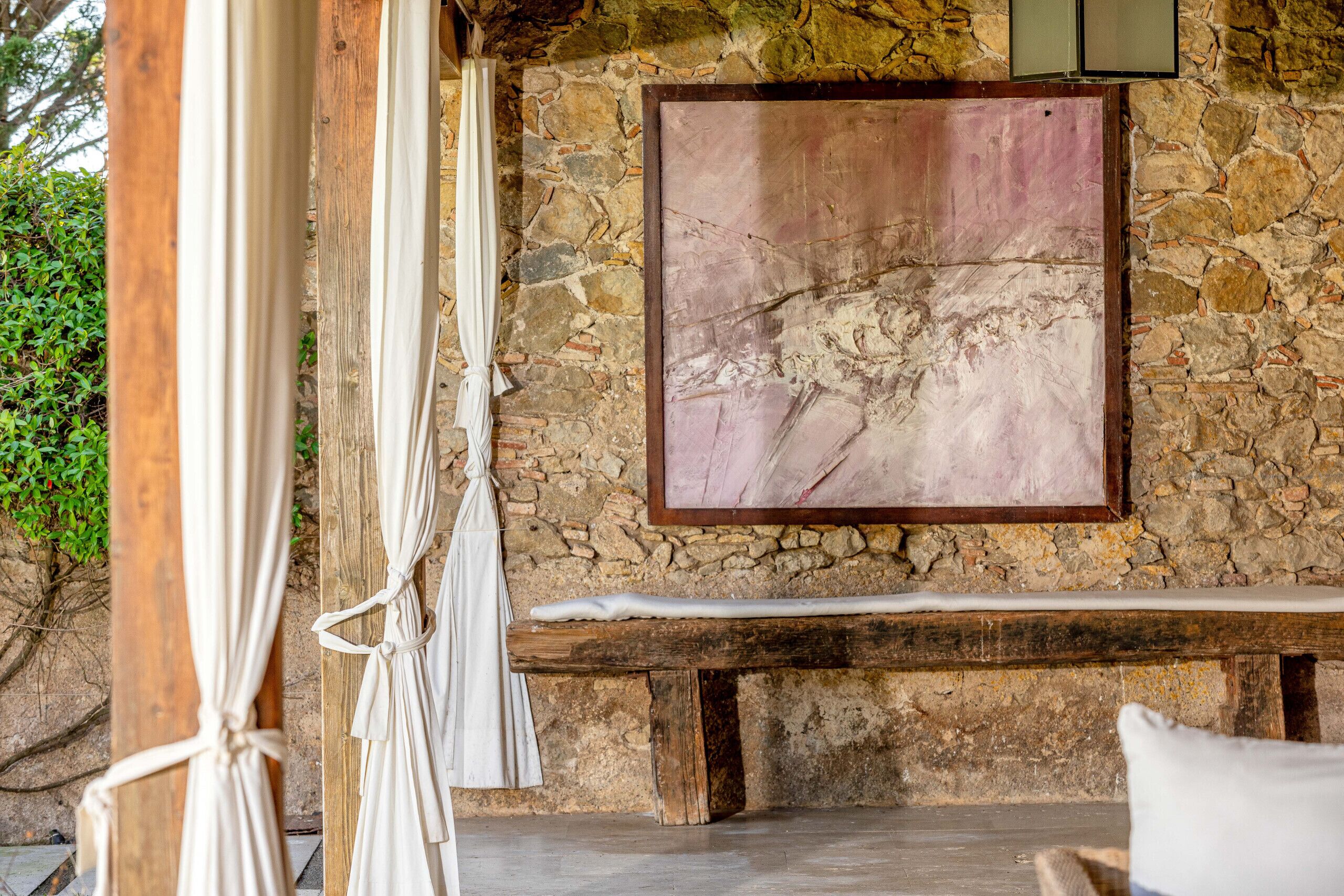 A stone wall with a large painting, a wooden bench, and a white curtain.