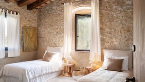 Ein Schlafzimmer mit zwei Betten, Steinwänden und einem großen Fenster mit Vorhängen.