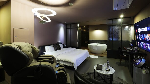 A modern hotel room with a bed, massage chair, bathtub, desk, and a TV. - Desing Hotel Vine (Ansan)