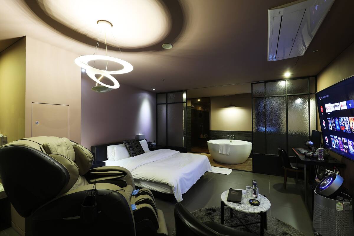 A modern hotel room with a bed, massage chair, bathtub, desk, and a TV.
