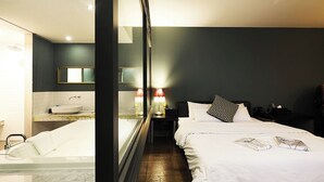 A modern hotel room with a large bed, a separate bathroom with a bathtub, and a nightstand with a lamp. - Desing Hotel Vine (Ansan)