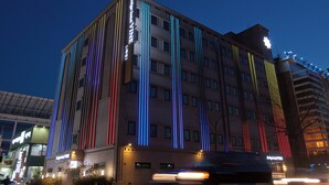 A multi-story hotel with vertical light strips on the facade, a visible entrance, and a parking area. - Desing Hotel Vine (Ansan)