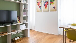 A modern living room with a flat-screen TV, a bookshelf, a dining table with chairs, and three colorful world maps on the wall. - Italianway Comfort - Salmini 1 (Milan)